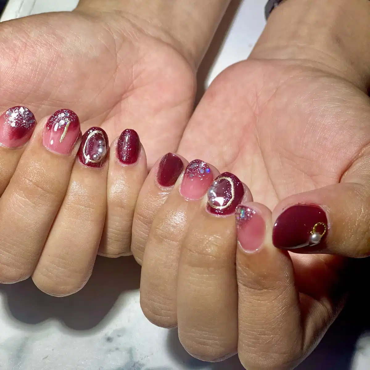 Short maroon nails with glitter fades and pearl-like accents