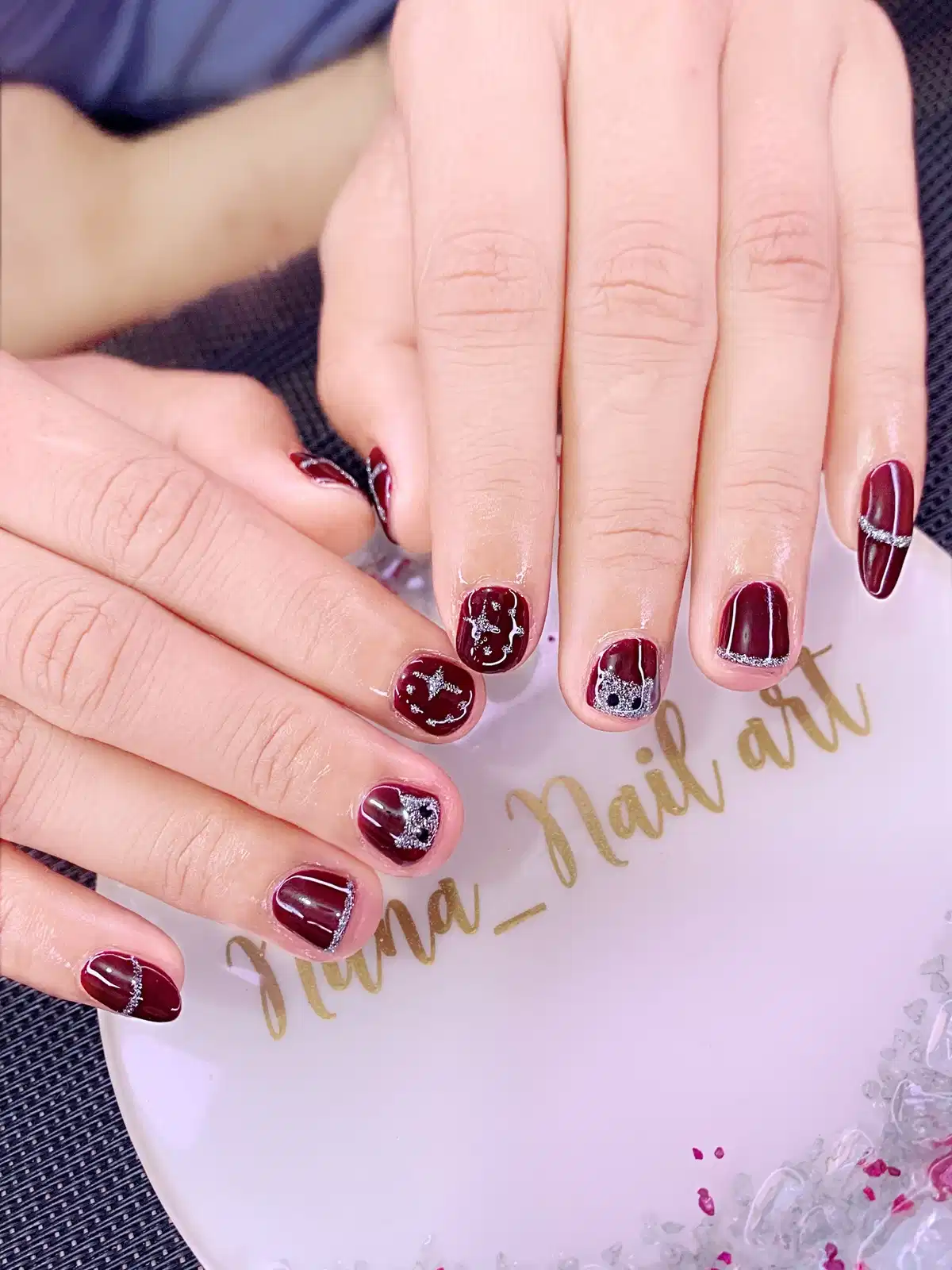 Short maroon nails with silver glitter tips and star accents