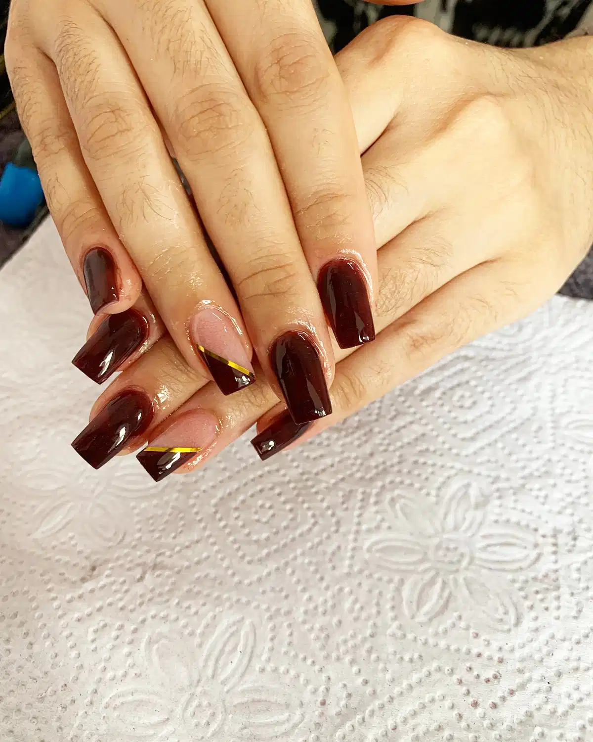 Deep maroon square nails with pink-and-gold diagonal accents