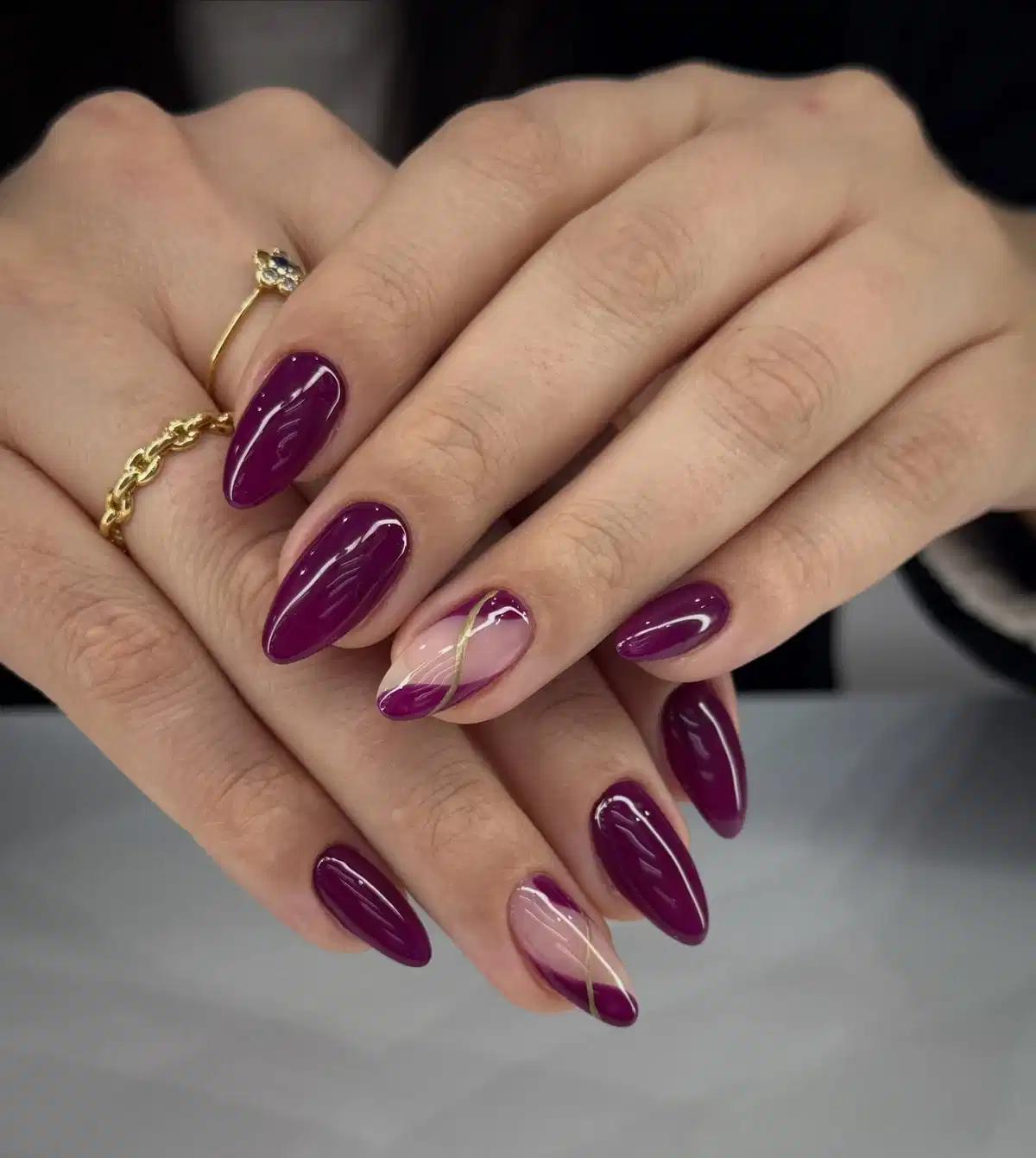 Deep plum nails with nude diagonal accents and thin gold striping