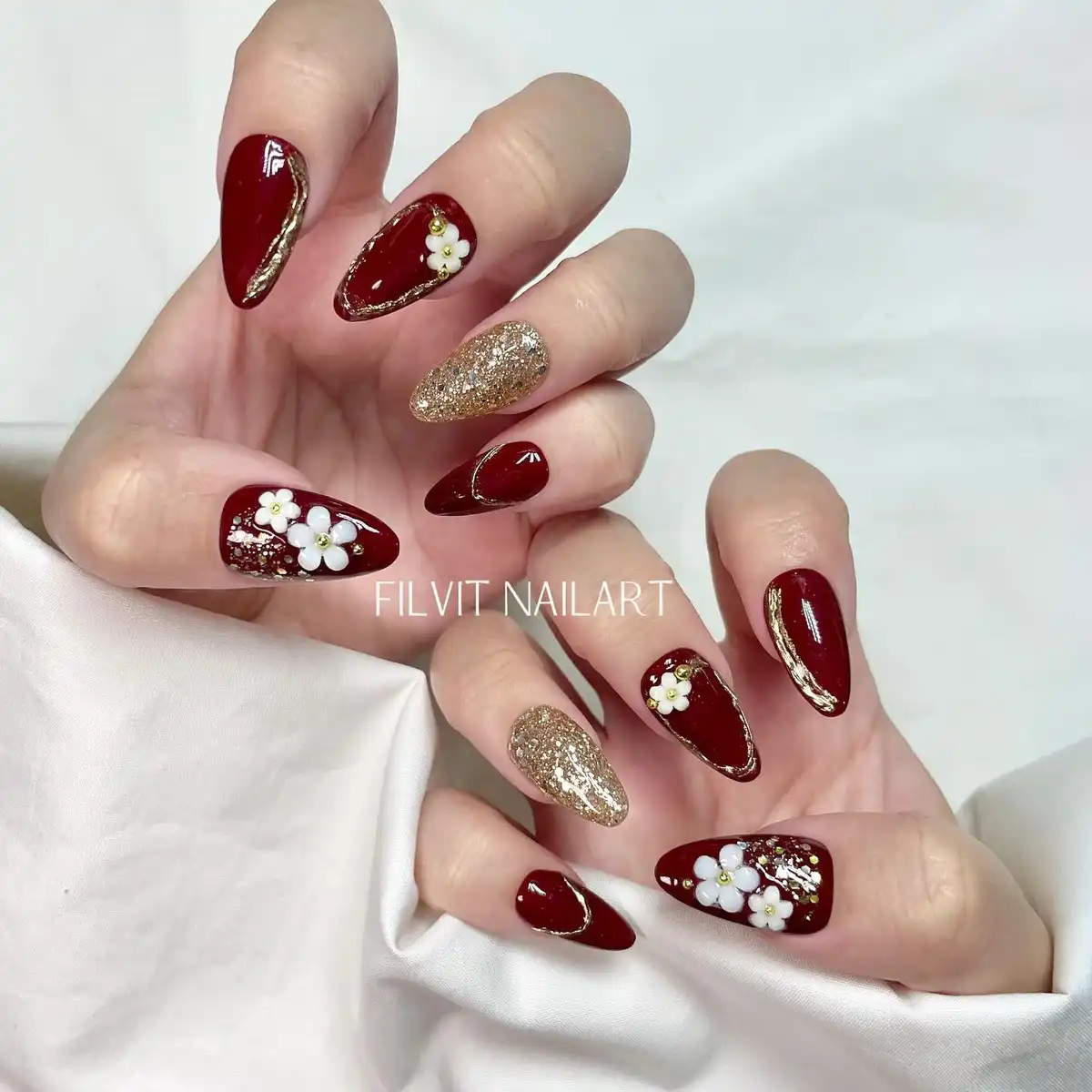 Maroon nails with gold glitter and raised white flowers