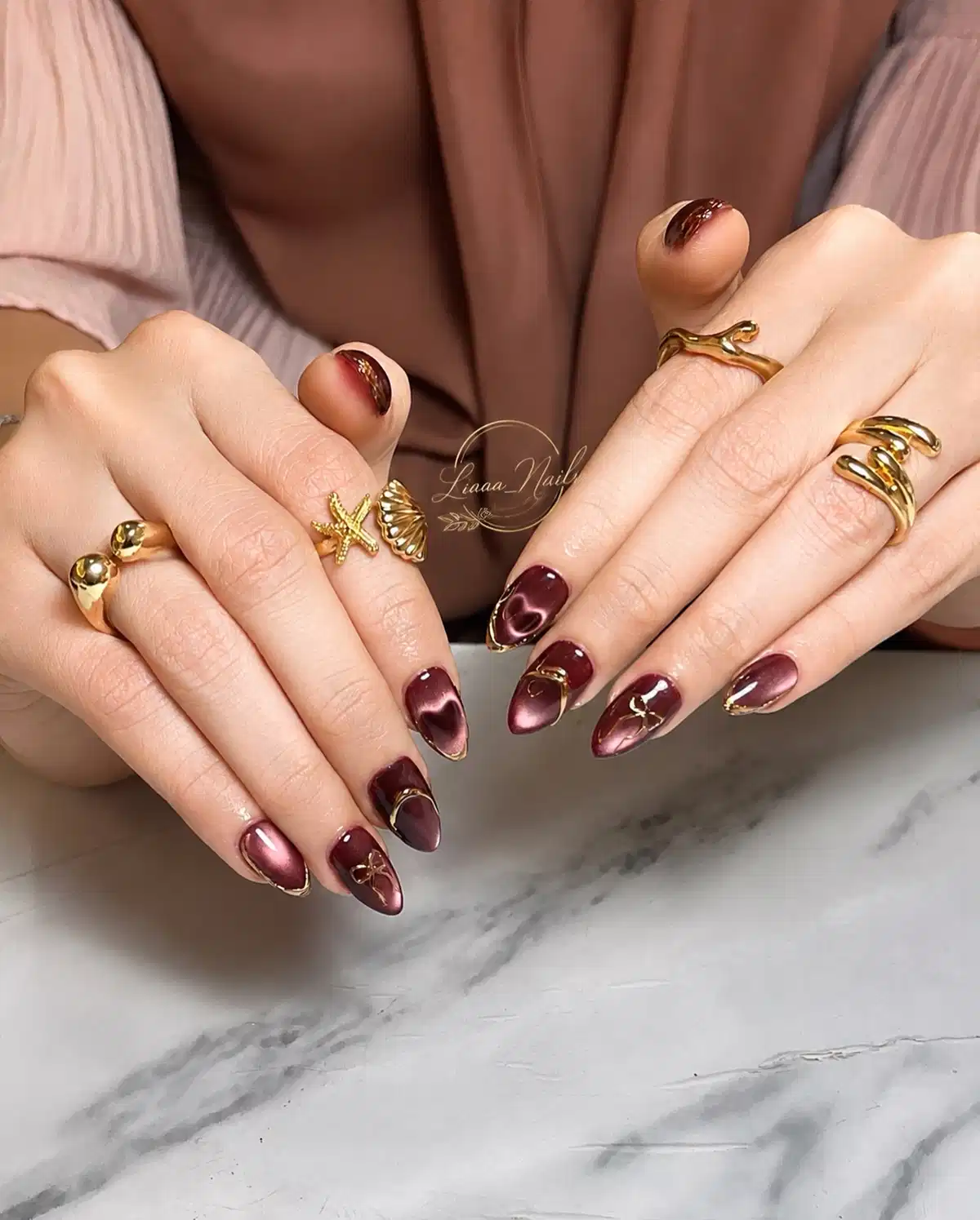 Metallic maroon pointed nails with gold edging