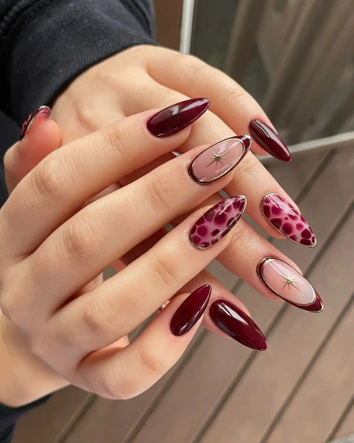 Maroon and nude pointed nails with metallic borders and star charms