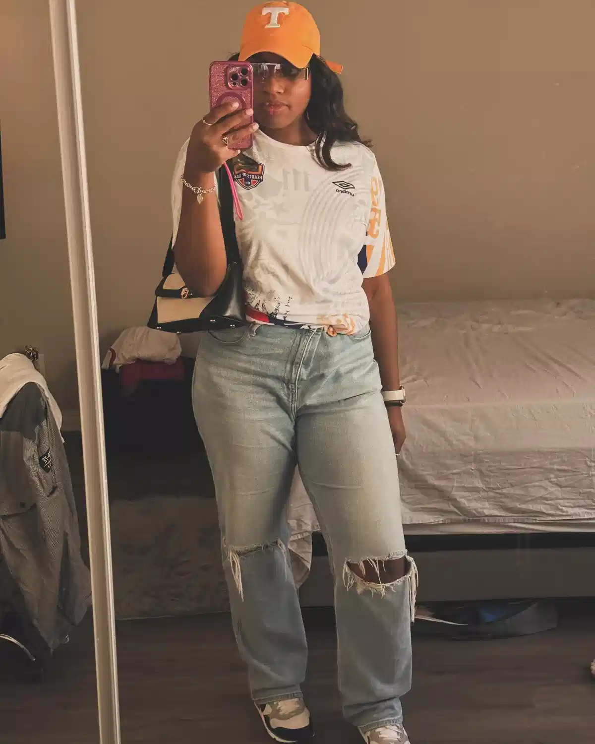 Orange ‘T’ cap with white graphic top and ripped light jeans