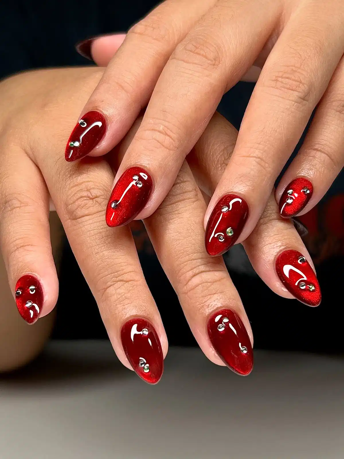 Shimmery red almond nails with rhinestone studs