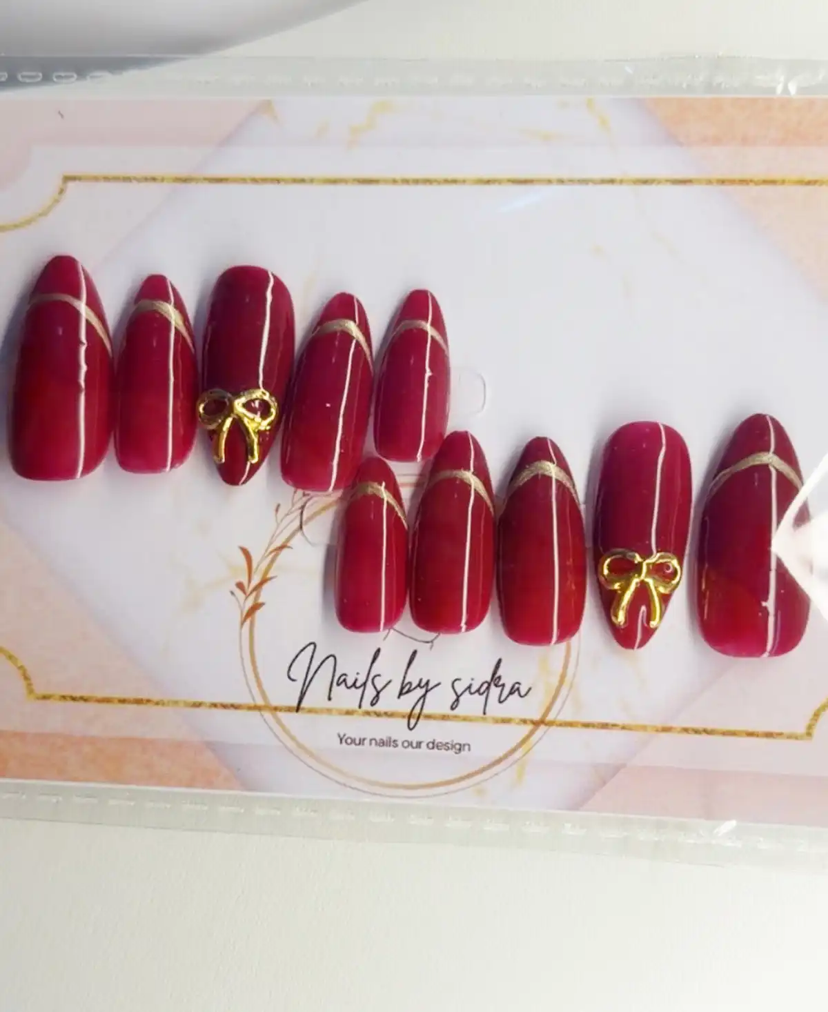 Maroon press-on set with thin gold diagonals and bow accents