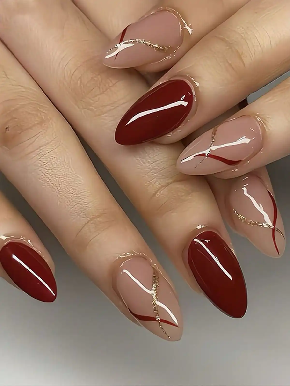 Glossy maroon and nude almonds with thin gold wave lines