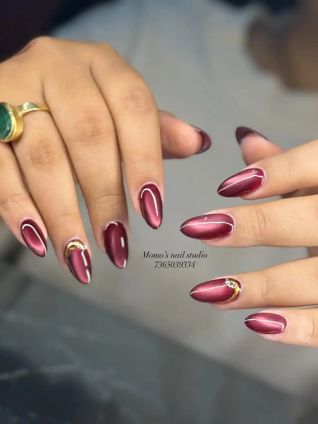 Metallic maroon almond nails with white outlines and gold cuticle accents