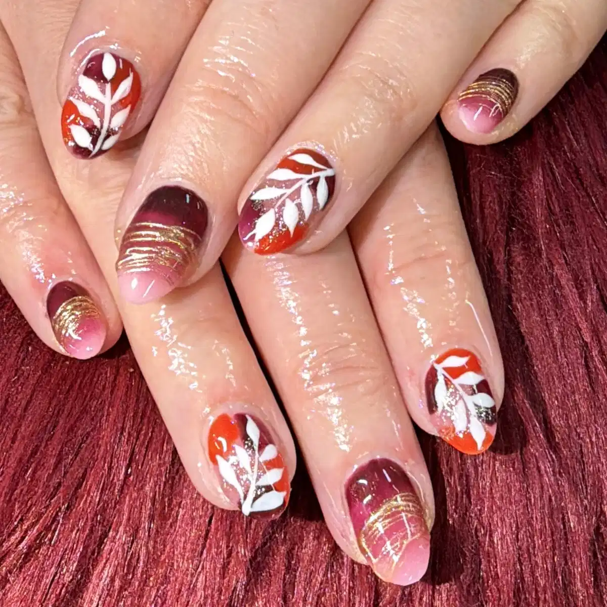 Short multicolor nails with white leaf motifs and fine gold line accents