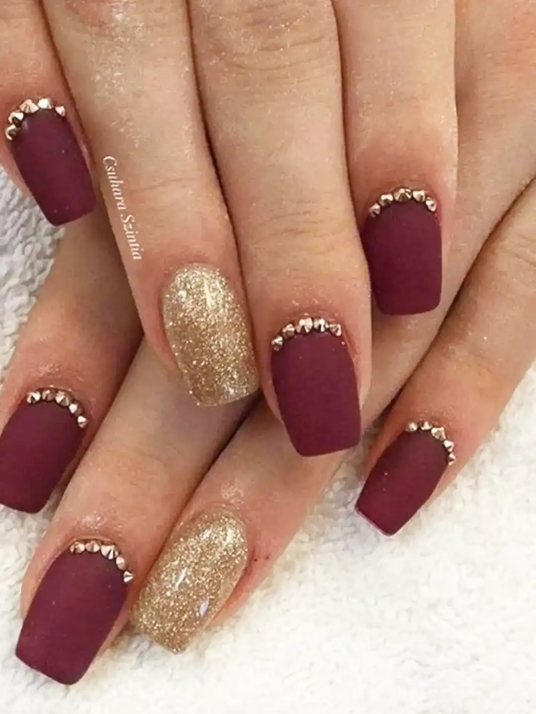 Matte maroon squares with gold glitter accents and cuticle studs