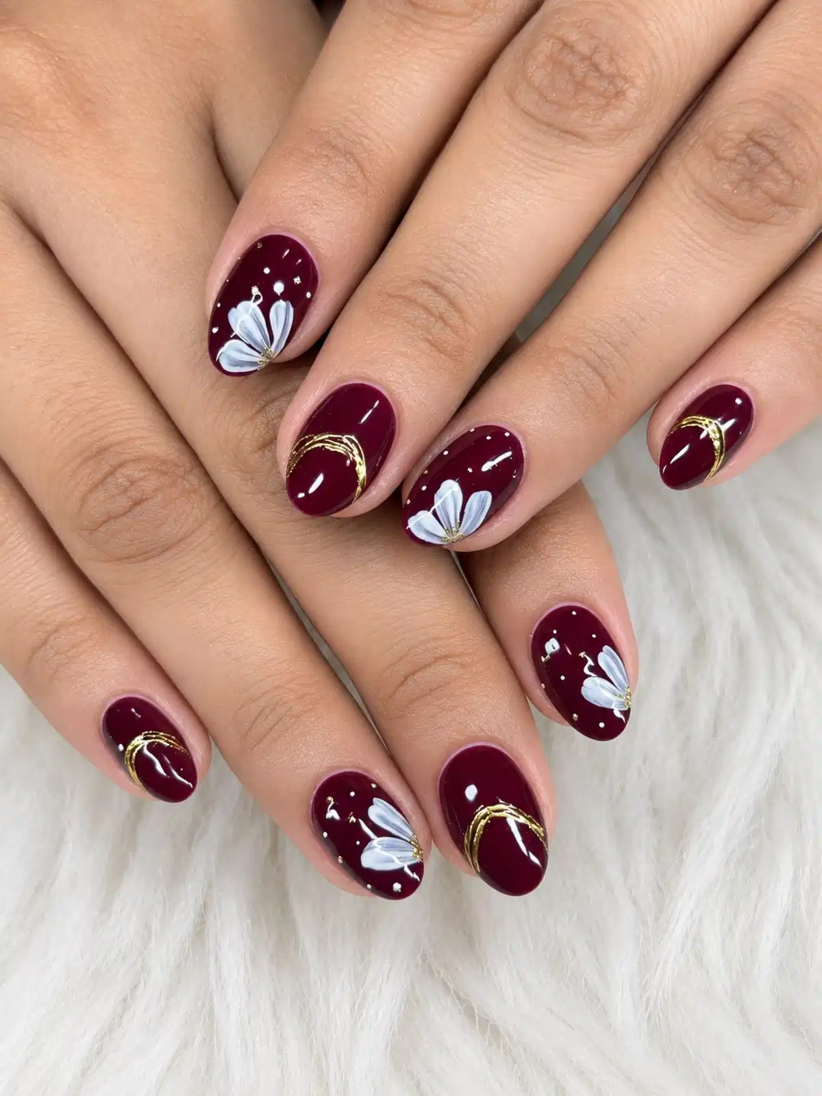 Maroon nails with white flowers, dots, and gold curves