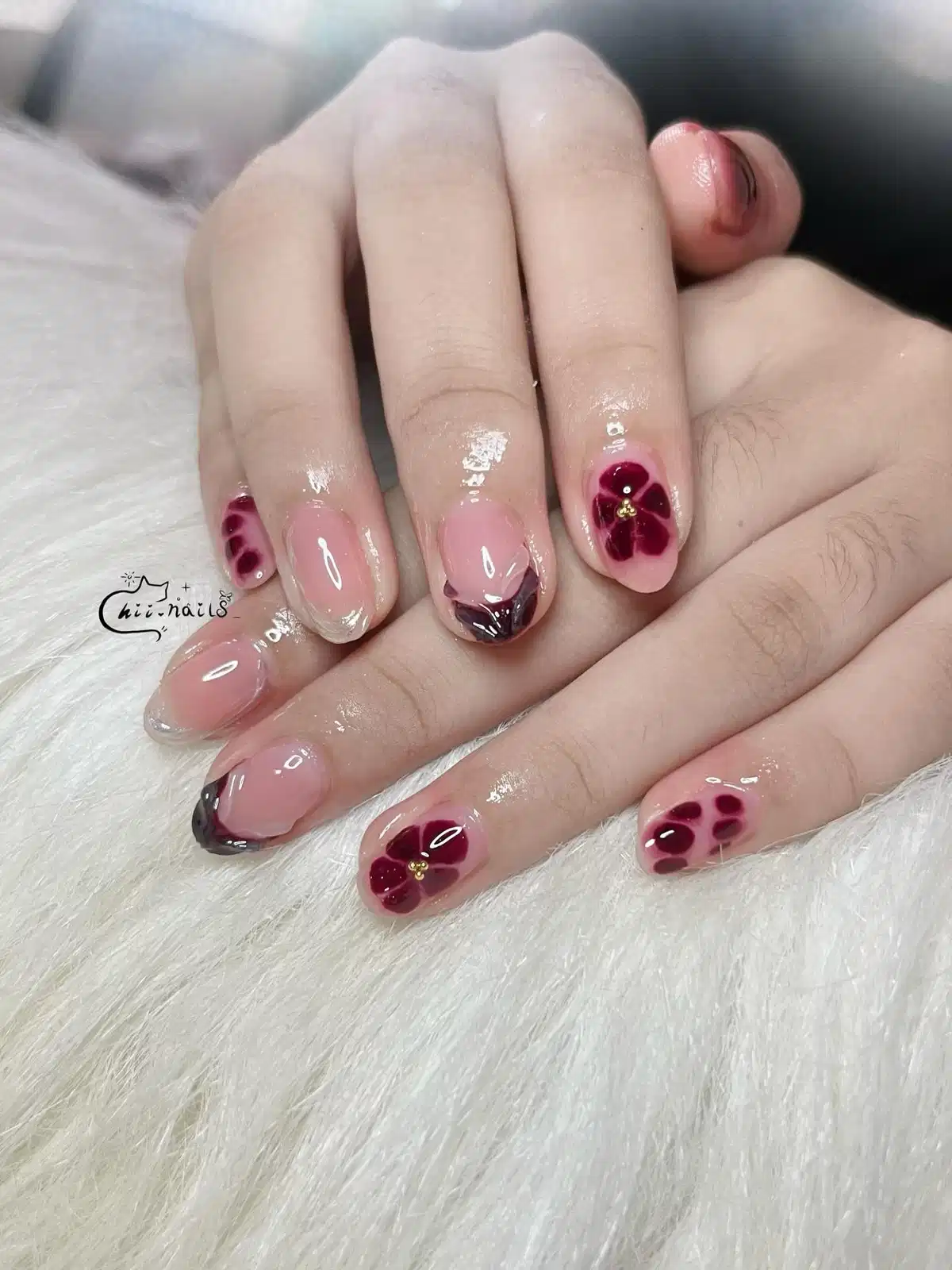 Sheer pink nails with maroon floral motifs and small gold centers