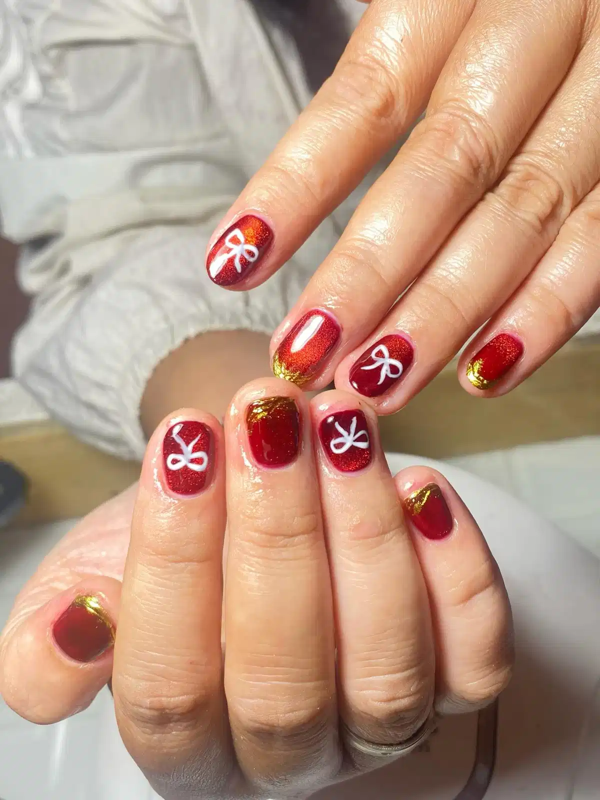 Shimmery red short nails with white bow art and gold foil tips