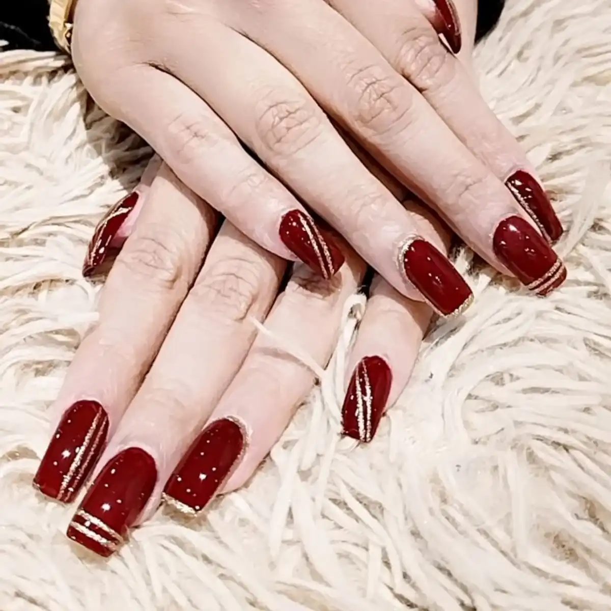 Glossy maroon square nails with thin gold striping