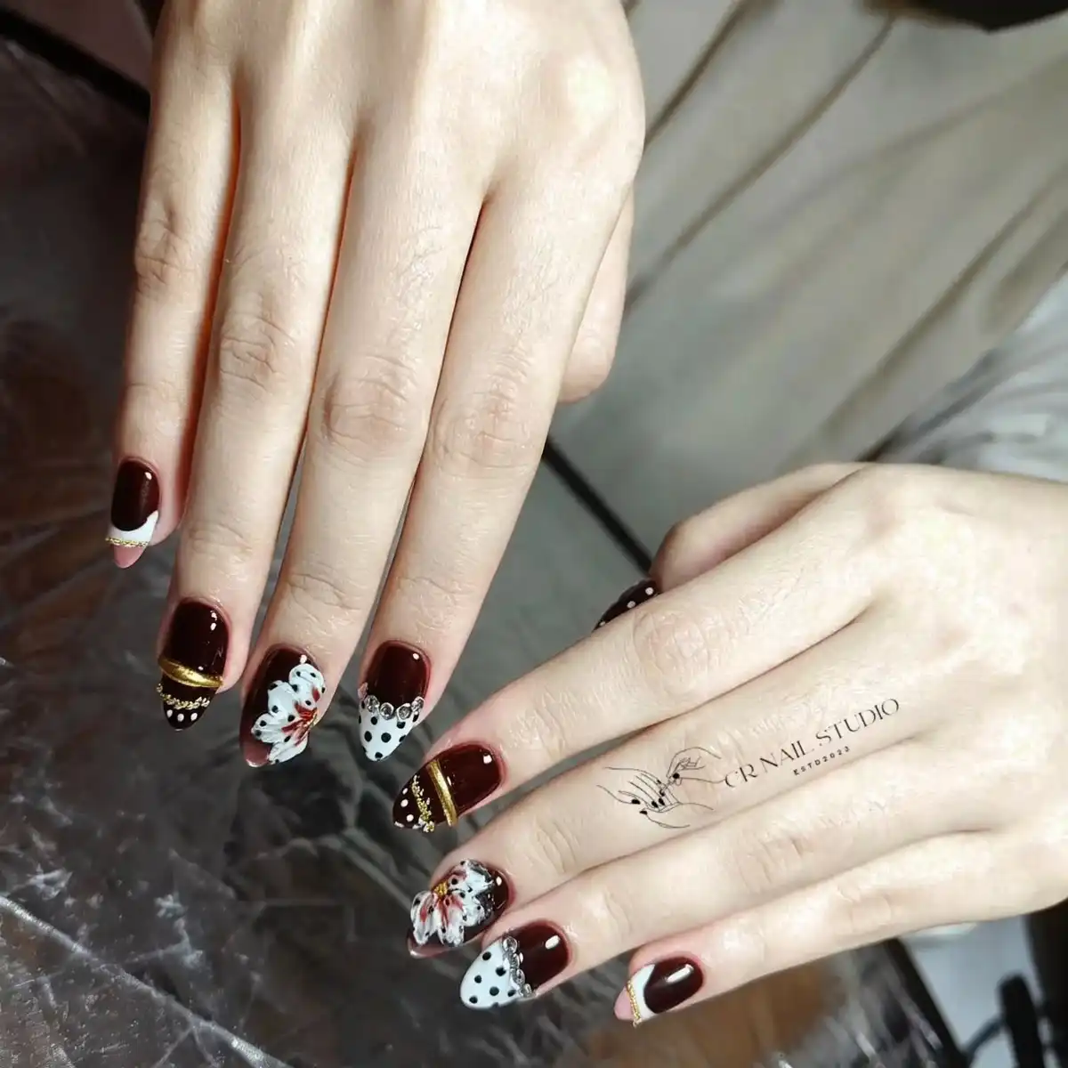 Burgundy nails with polka-dot accents, rhinestones, and gold bands