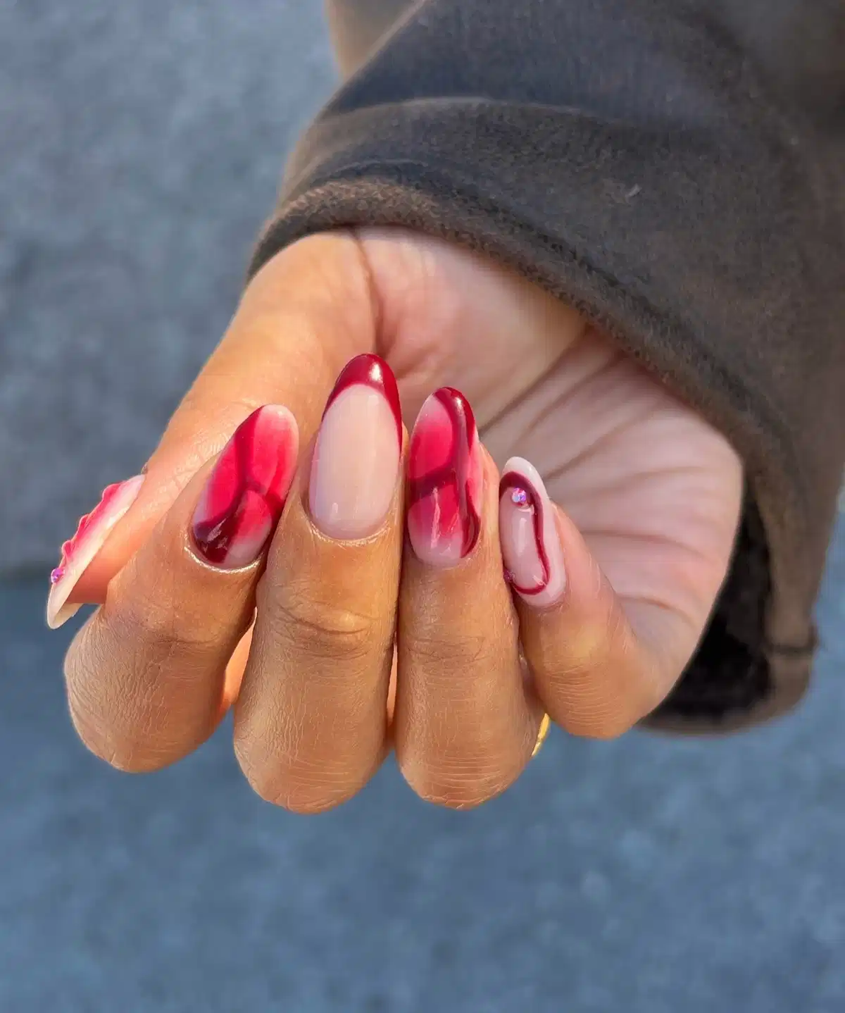 Nude almond nails with maroon abstract swirls and a rhinestone accent