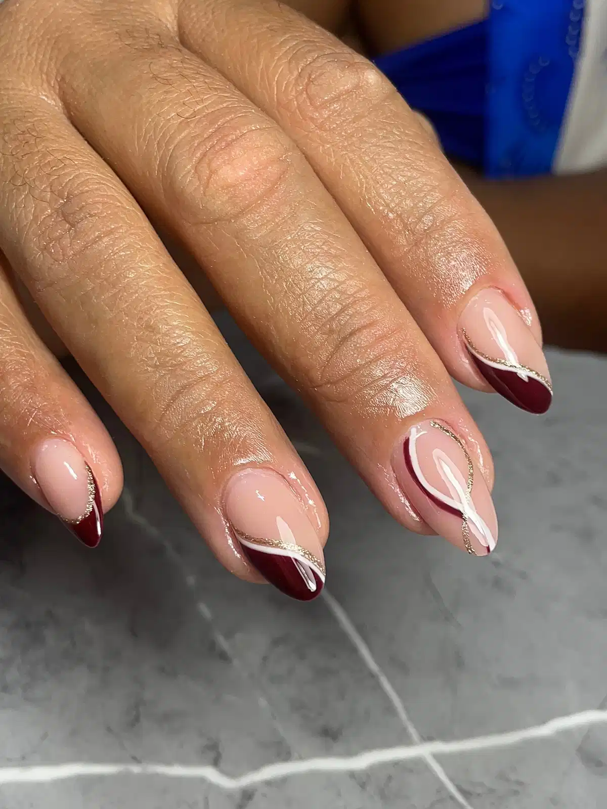 Nude base with maroon diagonal French tips and gold glitter lines