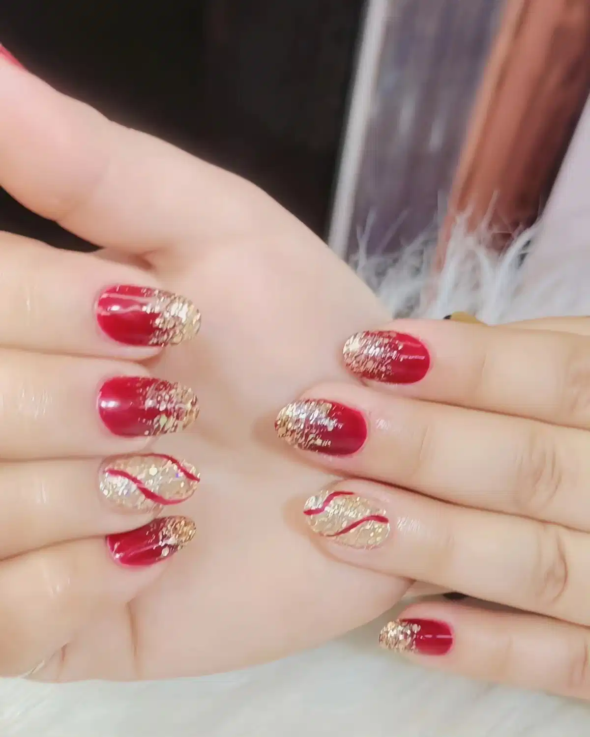 Red-maroon nails with gold glitter tips and wavy accent lines