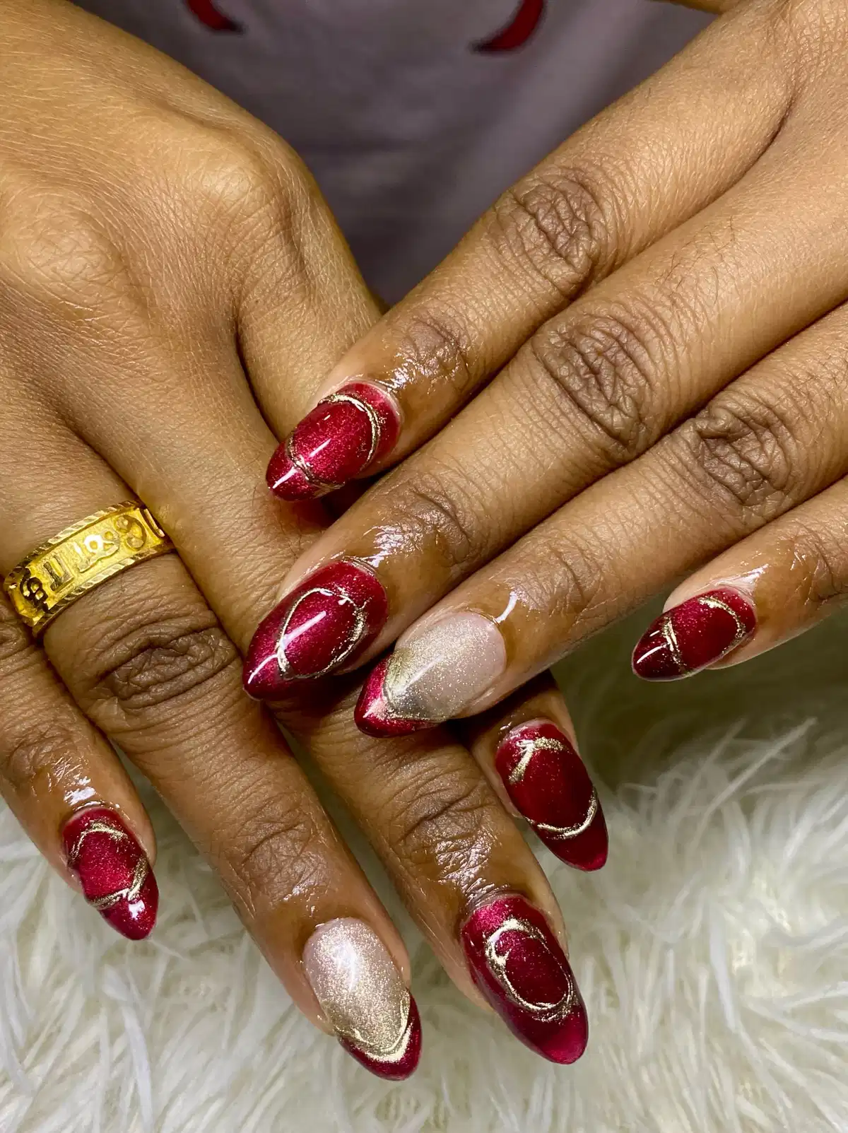 Sparkly maroon pointed nails with thin gold curves and shimmer accents