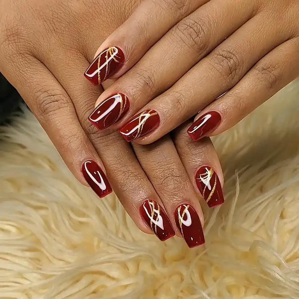 Glossy maroon square nails with thin gold swoop lines