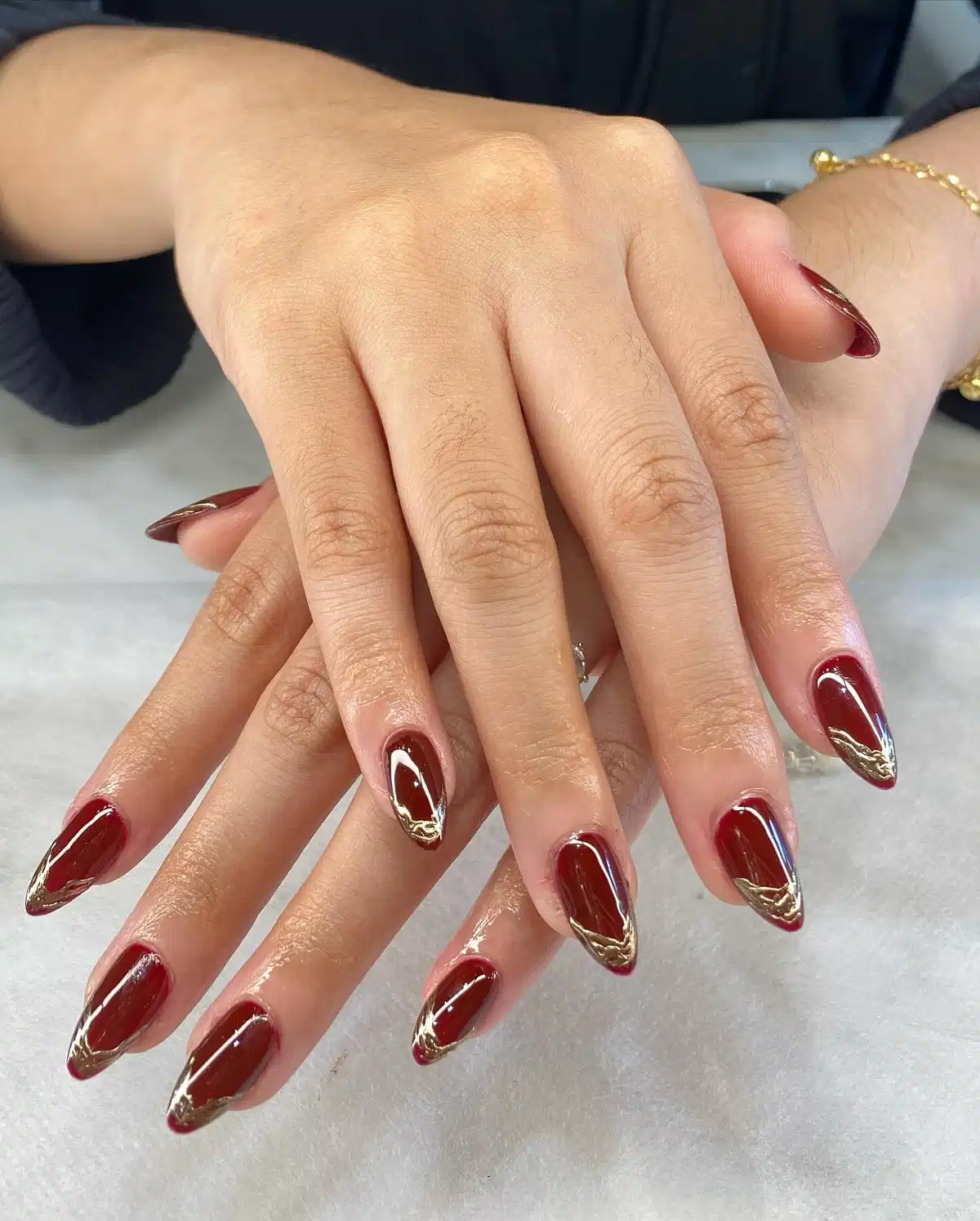 Glossy maroon almond nails with gold V-tip accents