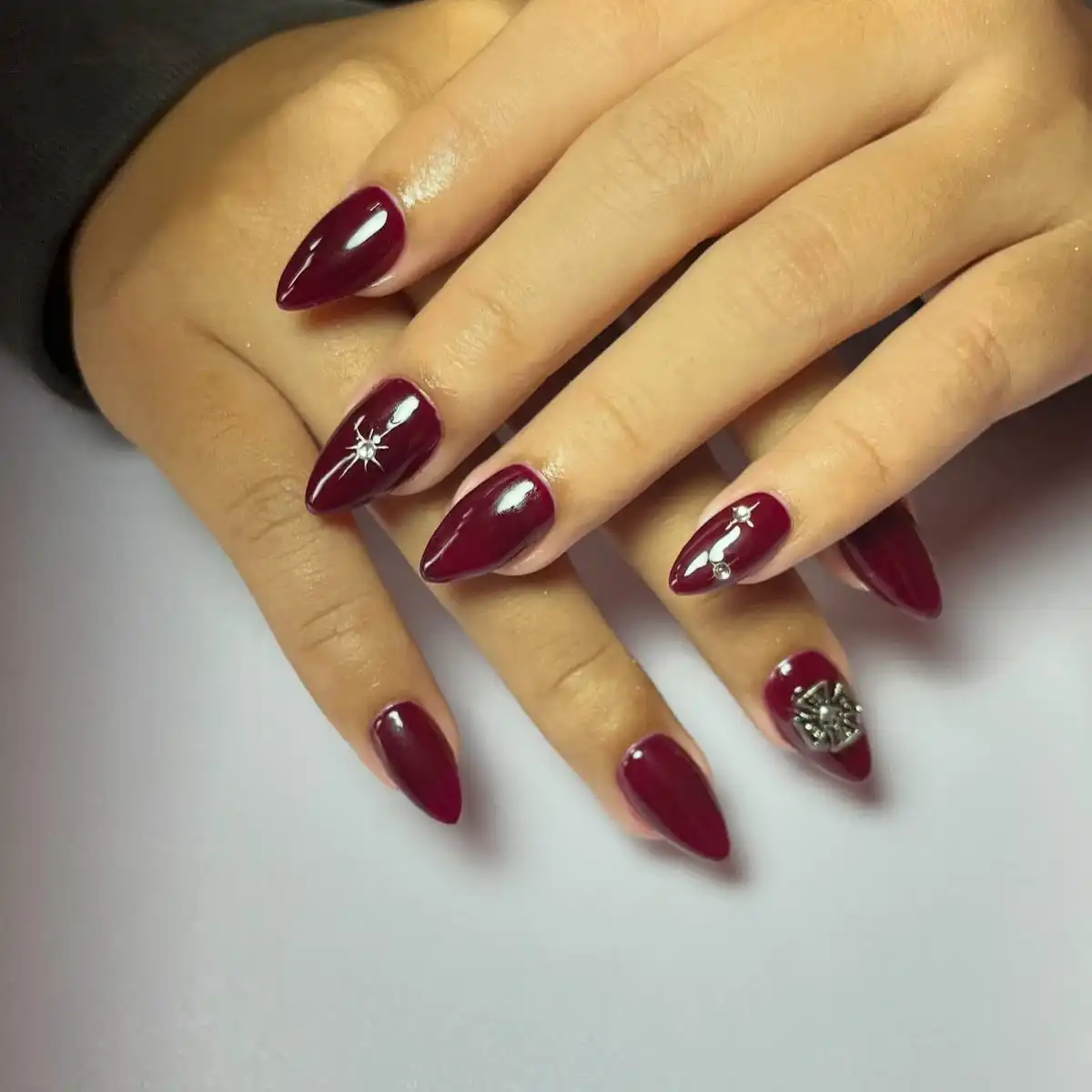Deep maroon pointed nails with silver rhinestone accents