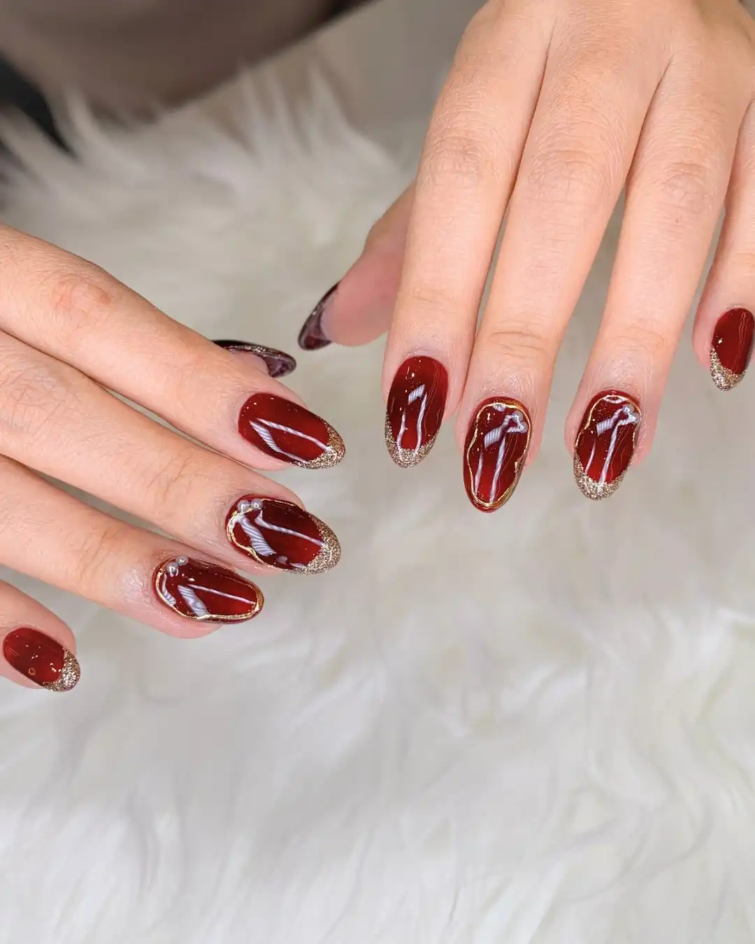 Glossy maroon with gold-glitter tips and thin gold oval outlines