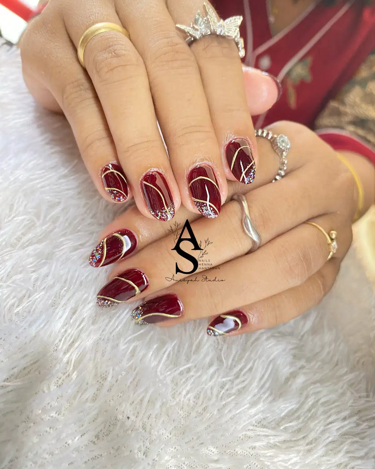 Short maroon nails with gold striping and glittery tips