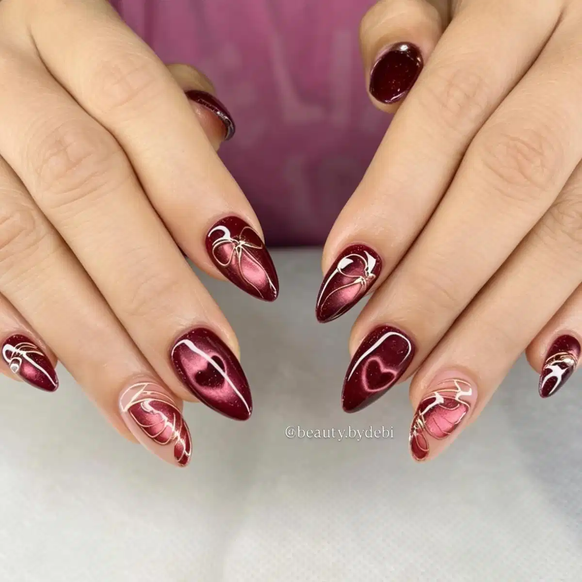 Glossy maroon almond nails with white line-art bows and heart detail