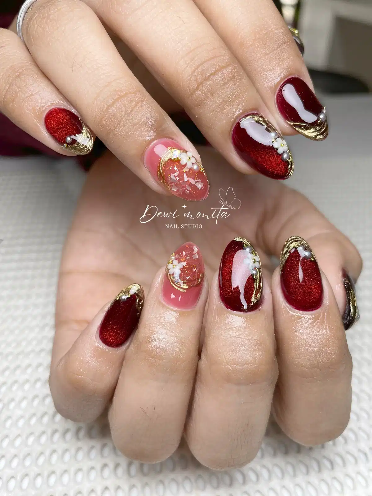 Shimmery maroon nails with gold edging, pearls, and floral accent