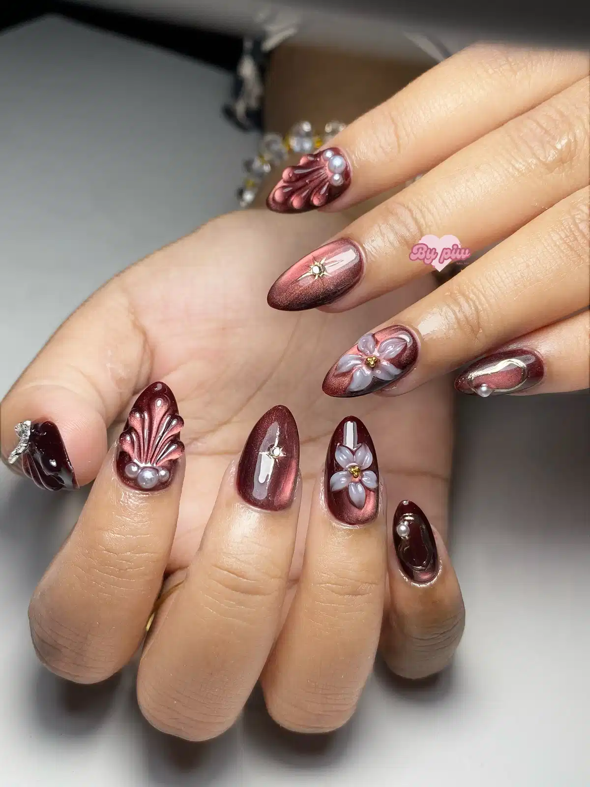 Metallic maroon nails with 3D florals, pearls, and sculpted ridges