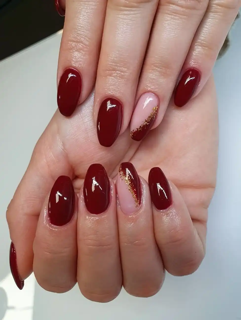 Glossy maroon ovals with diagonal nude accents and gold glitter stripe