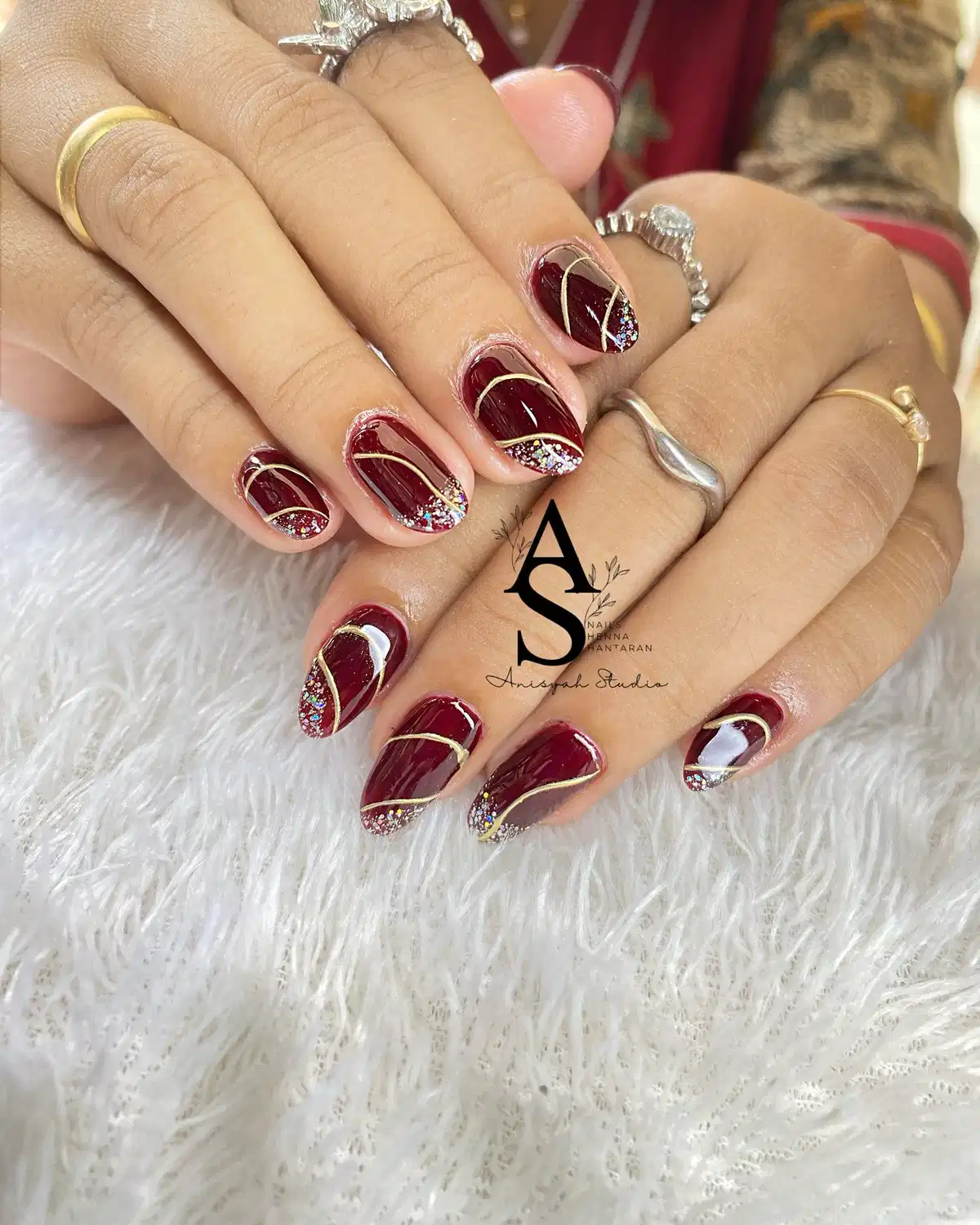 Maroon nails with sweeping gold lines and glittered tips