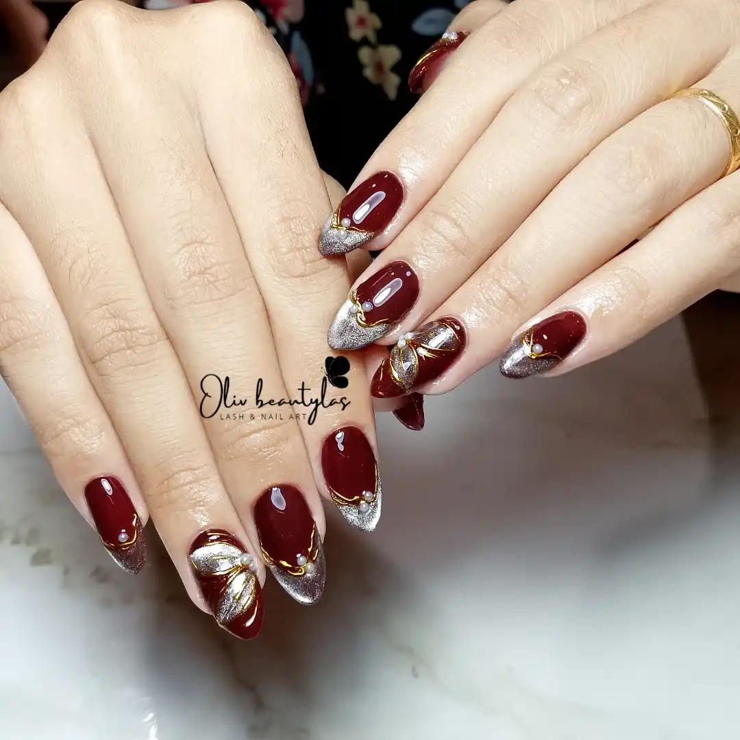 Maroon nails with silver-glitter tips, gold beads, and metallic accent