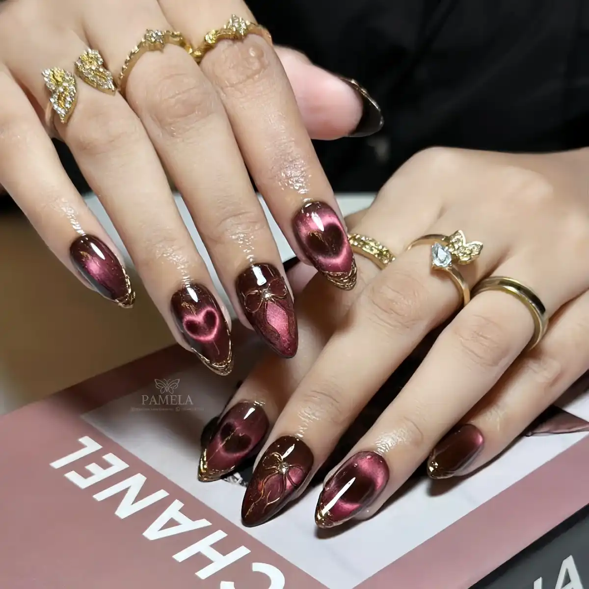 Dark maroon-brown nails with pink heart motifs and gold edging