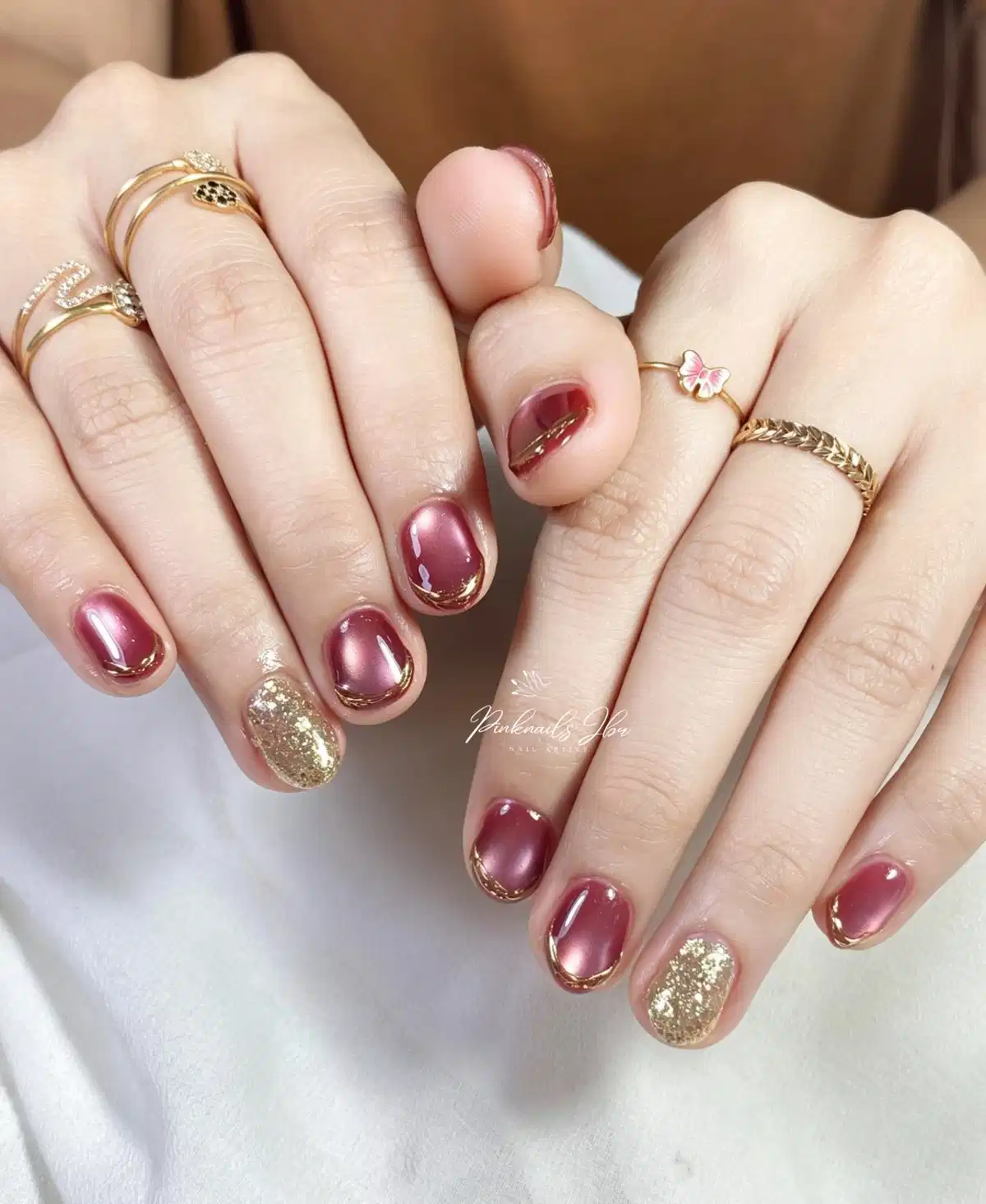 Mauve-maroon nails with metallic outlines and gold-glitter accents