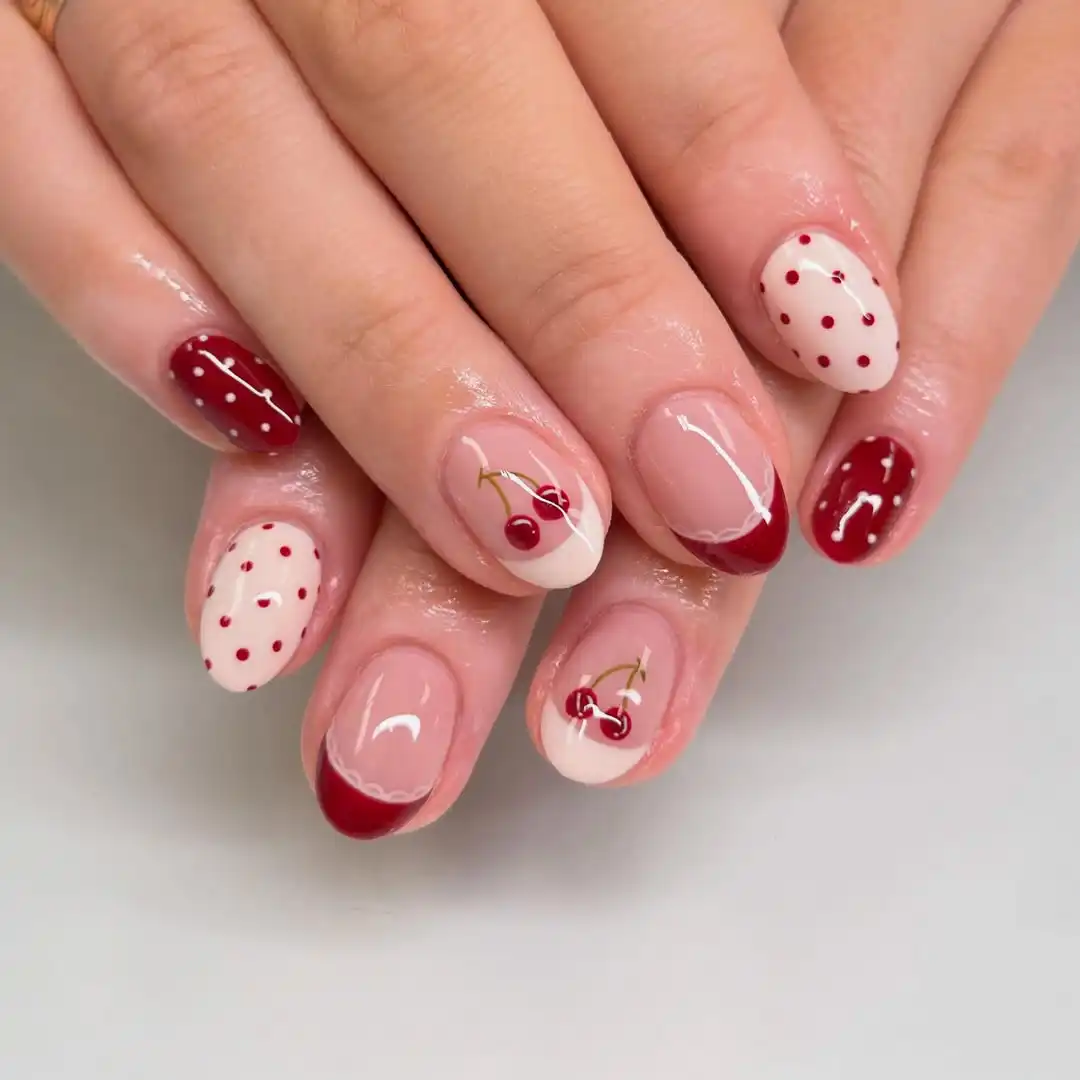 Short nude nails with maroon tips, polka dots, and cherry art