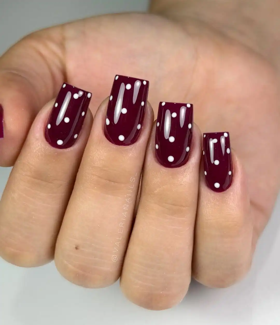 Glossy maroon nails with white polka dots