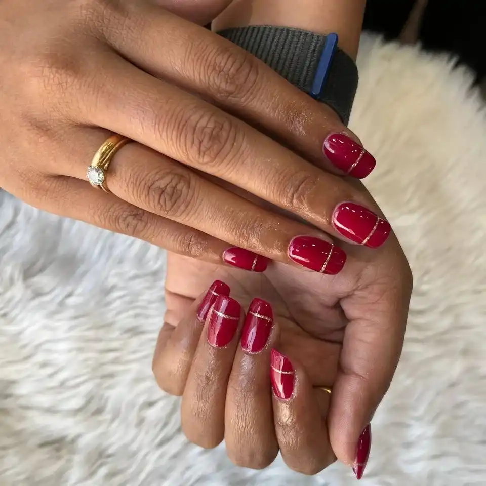 Maroon-red nails with thin gold stripe detail