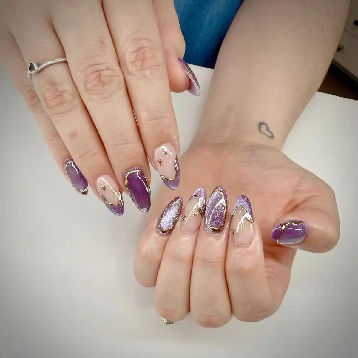 Purple metallic and nude nails with gold outline borders and starburst accents