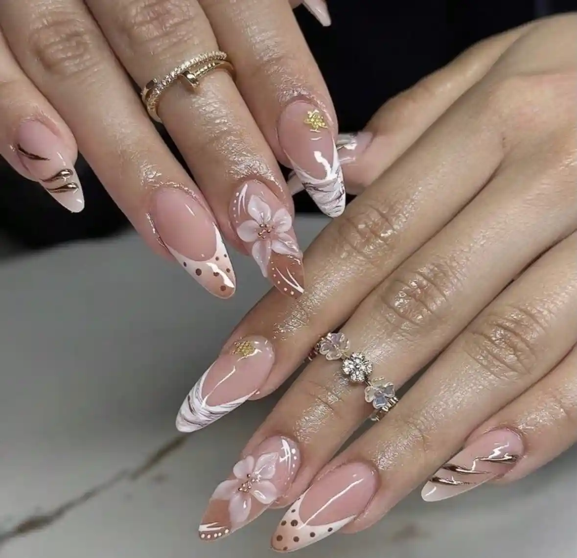 Nude stiletto nails with marbled tips, dotted accents, and raised flowers