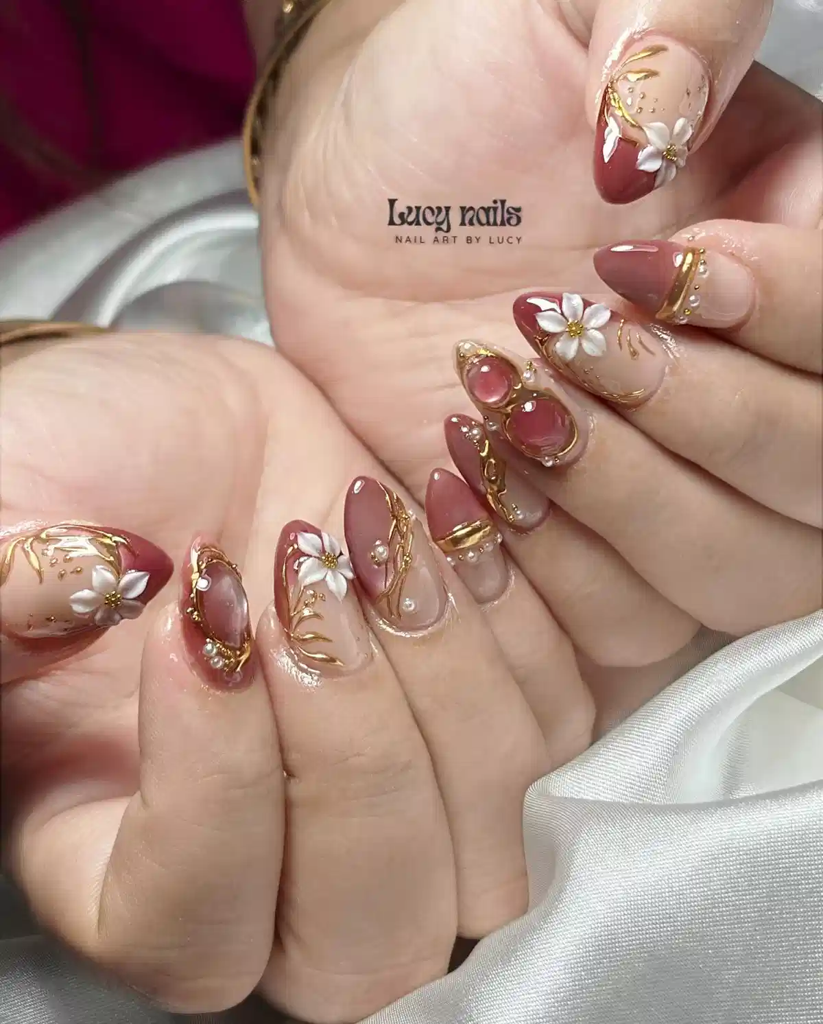Mauve and nude almond nails with gold linework, 3D flowers, and gem accents