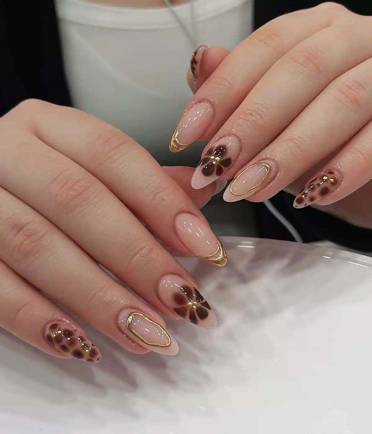 Nude almond nails with gold framing, brown florals, and spotted accents