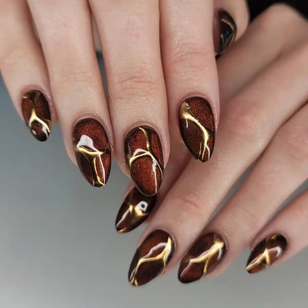 Shimmery brown nails with abstract gold linework and white accents