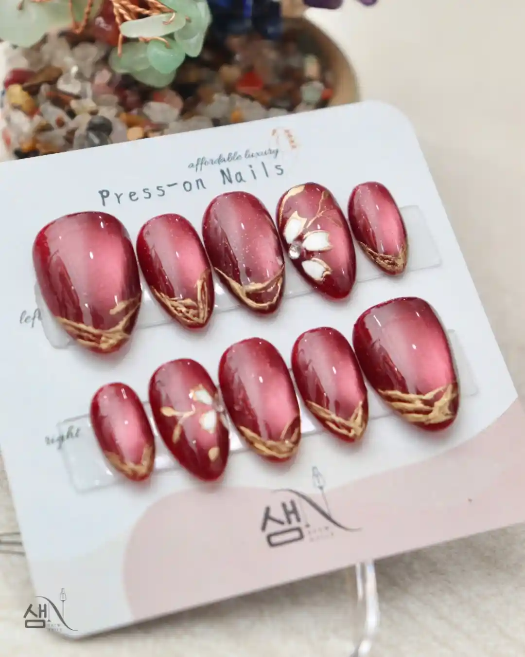Red-pink press-on set with gold V-tips and white petal accents