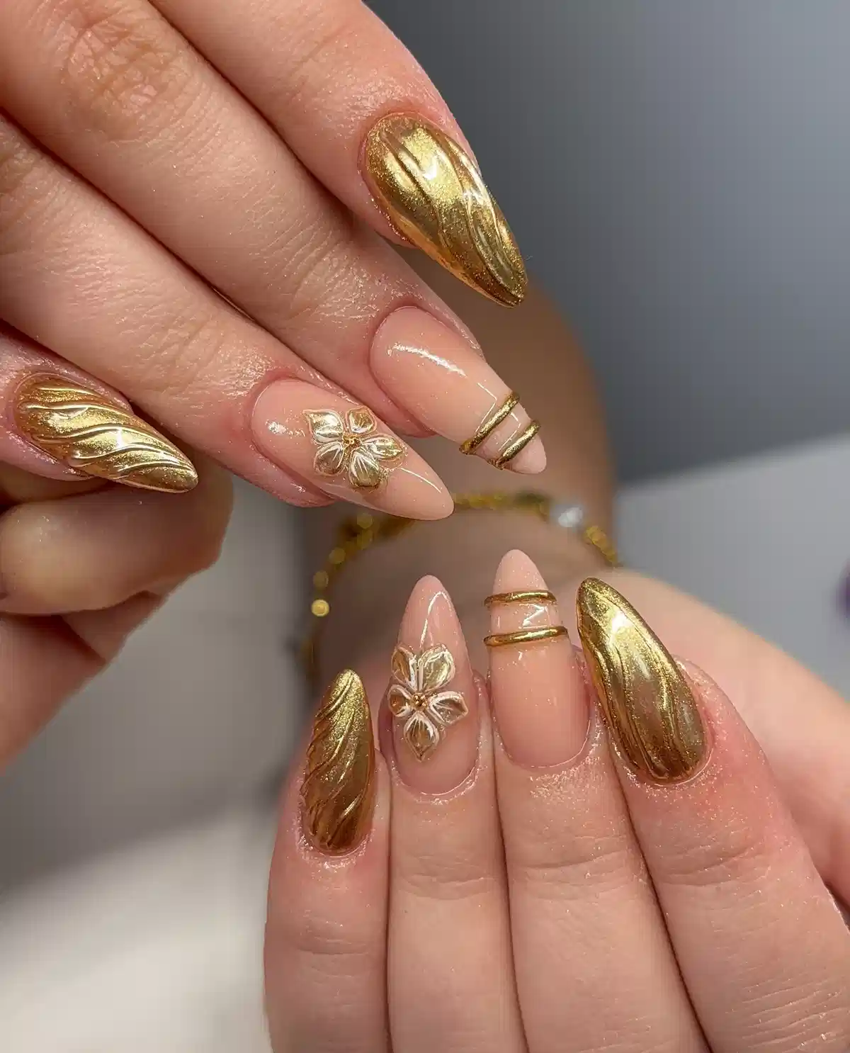 Nude almond nails with textured metallic-gold accents and floral detail