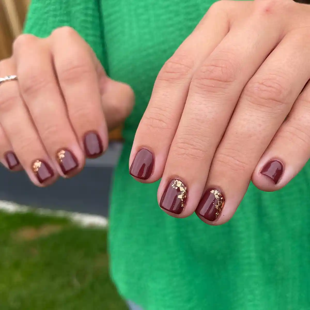 Glossy burgundy nails with small gold foil accents