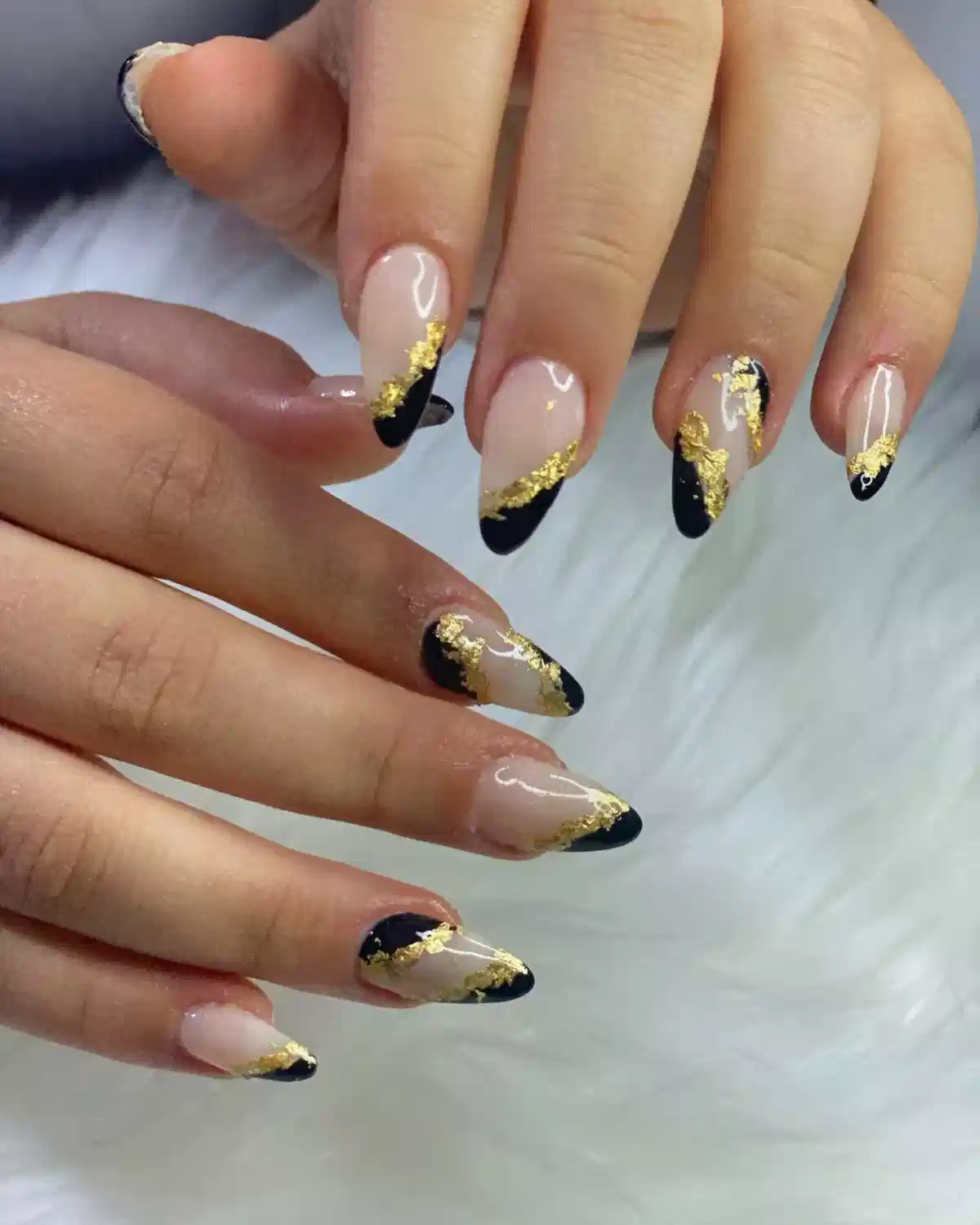 Nude almond nails with black angled tips and gold edging