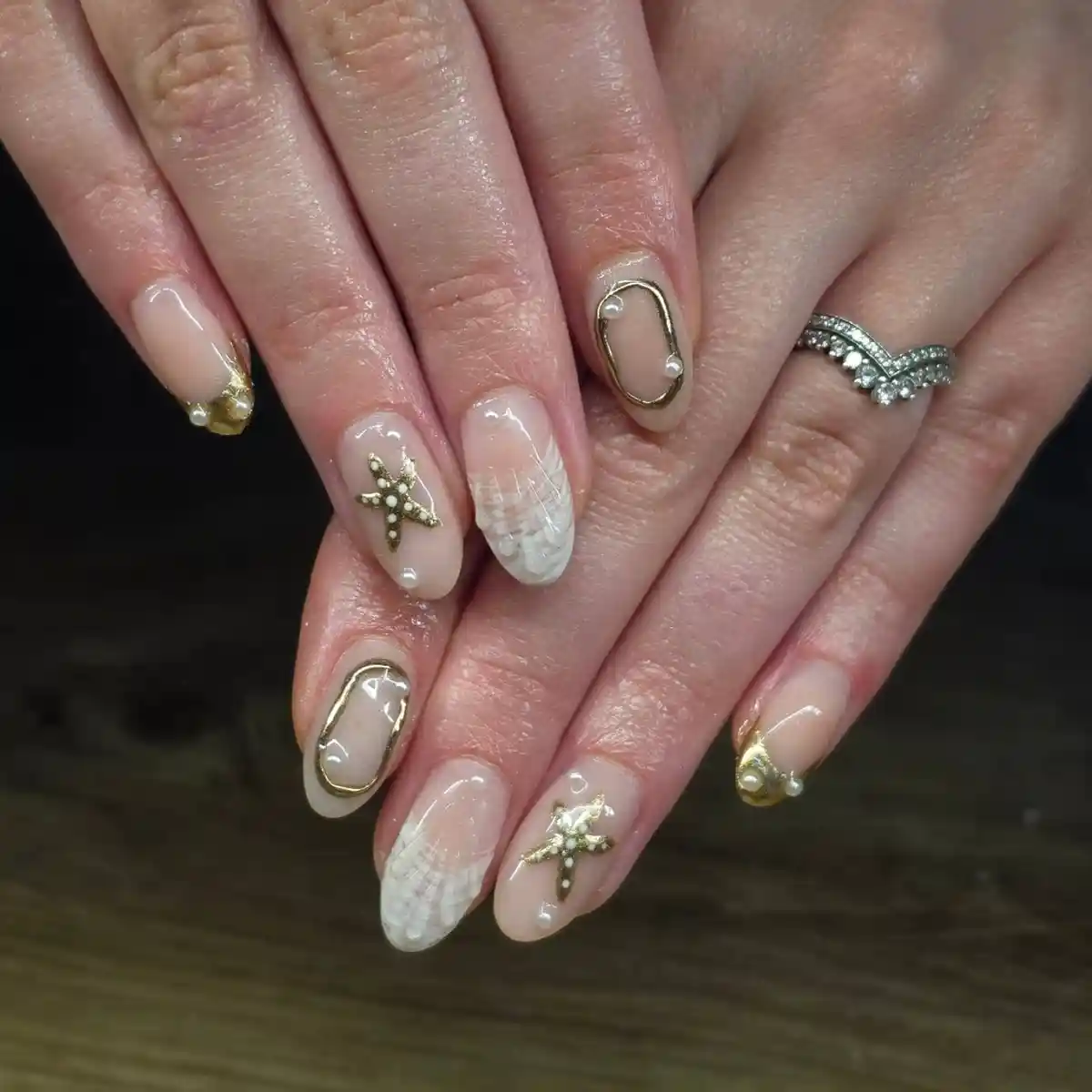 Nude nails with gold outlines, starfish accents, and white textured details