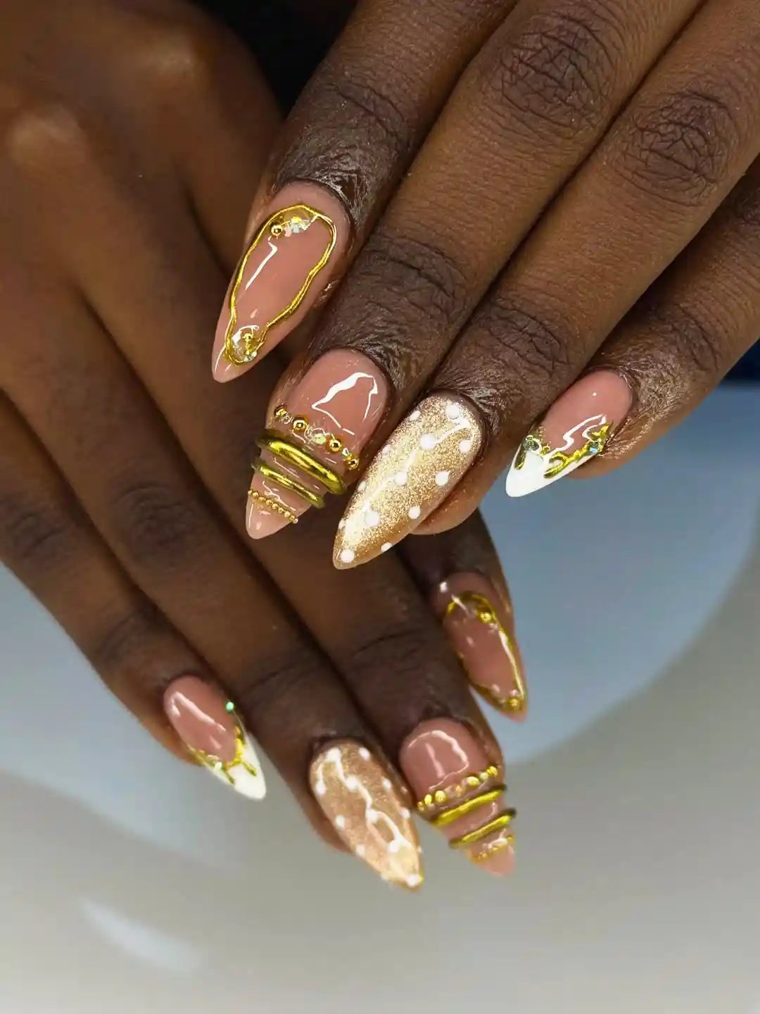 Nude almond nails with gold glitter accent, gold bands, and white-and-gold tips